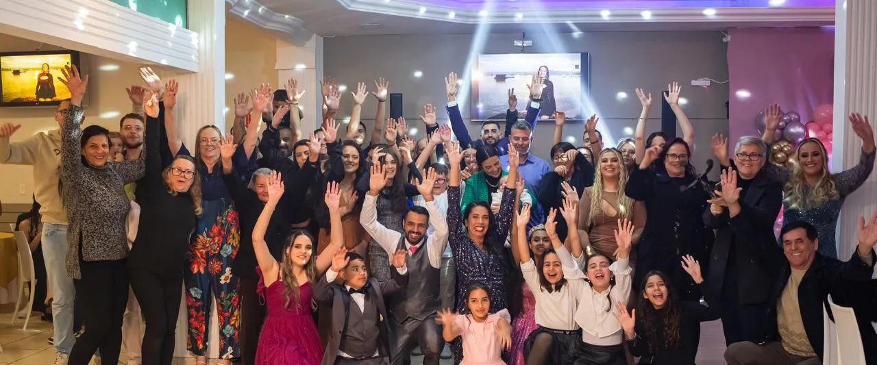 Convidados de mãos levantadas comemorando no salão do Ateliê da Festa