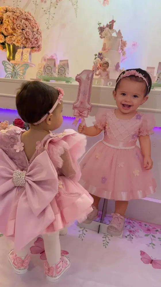 Duas bebês de vestido rosa na festa de primeiro aninho, diante da mesa decorada com borboletas