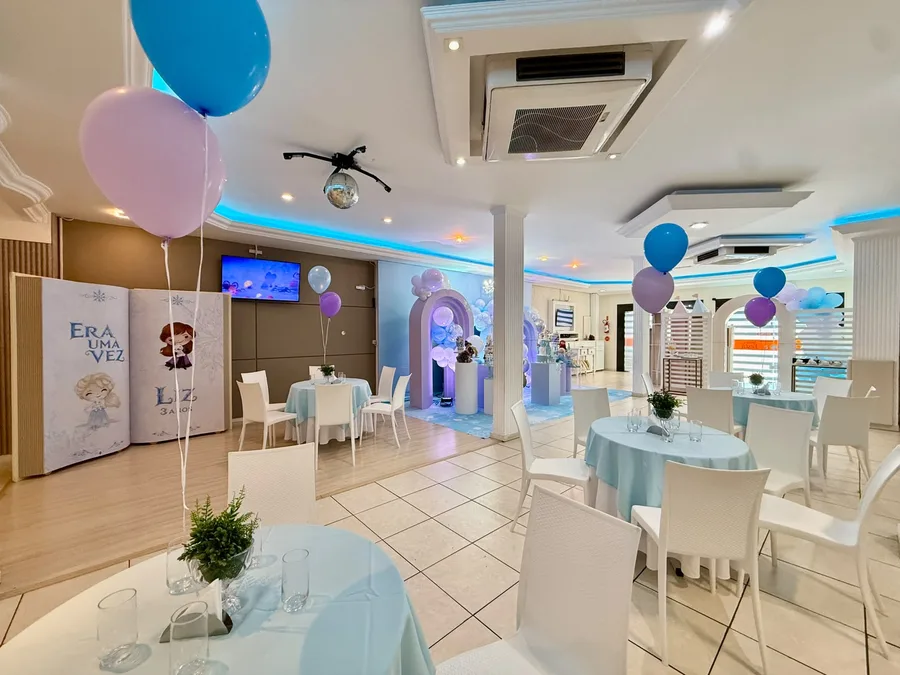 Salão decorado com tema Frozen, arcos de balões azuis e lilás e mesas postas